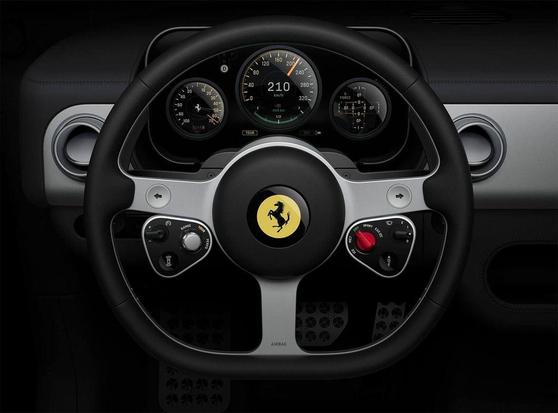 A head-on view of a Ferrari steering wheel, showcasing the emblem, buttons, and digital dashboard displaying speed and other metrics.