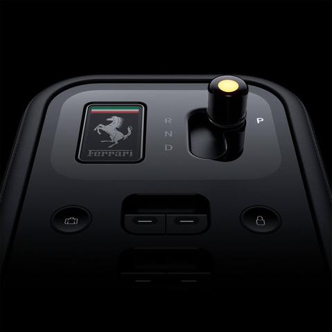 Close-up of a Ferrari gear shift console, featuring a black finish, buttons for park, reverse, neutral, and drive, with the Ferrari logo prominently displayed.
