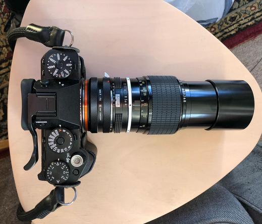 An overhead view of the Fujifilm X-T5, a Fuji X to Nikon F adapter, the 200mm NIKKOR tele lens, and the extended hood.