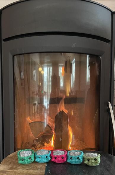 5 kleine gehäkelte unfertige dumpsterfire vor einem Kamin mit Schaufenster. Zur Fertigstellung fehlen nur noch die Flammen.