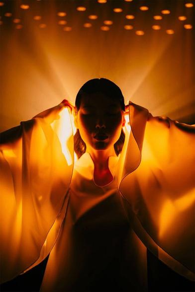 A person  in a flowing white dress, illuminated by warm, golden lights, creating a dramatic and ethereal atmosphere.