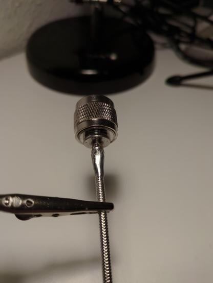 A silver N-connector soldered to a non-shielded RG402 coax cable, it is held by a small metal clamp on top of a white desk.