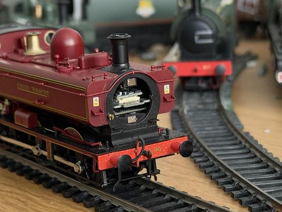 Close up of a maroon Pannier tank engine model. The smoke box door is missing, showing the internal circuitry.