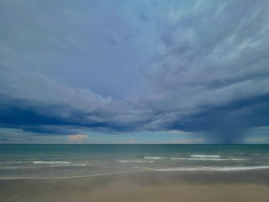 A shot of the Atlantic Ocean from Hillsboro Beach, Florida. The water is light blue, but becomes darker as it gets deeper. The sky has large clouds which are a mixture of grey to dark blue. The weather looks ominous.