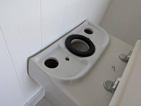 The base of a toilet showing two small and two large holes into the cavity inside the base, with no access to hold nuts under the small holes while screwing the bolt into them.