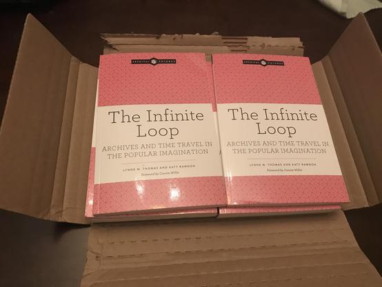 Two stacks of The Infinite Loop: Archives and Time Travel in the Popular Imagination by Lynne M. Thomas and Katy Rawdon. The cover has a bright salmon pink design.