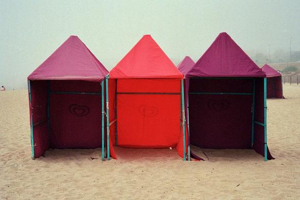 A foggy afternoon on an Atlantic beach. Three tents alternate colours: purple, red, purple.
