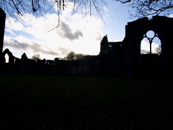 Ruined abbey in shadow with a cloud that resembles a flying dragon above it.