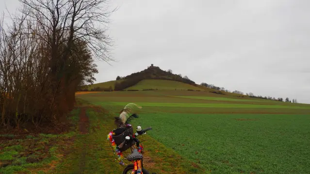 Desenberg mit Ruine auf dem Gipfel, davor ein Fahrrad auf einem Feldweg