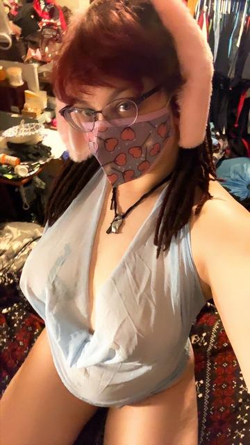 Bunnii sits on his heels looking at the camera from behind a cute lollipop face mask, with soft pink bunny ears & a sheer pastel blue negligée that shows off his tits & the curve of his belly above bare thighs.