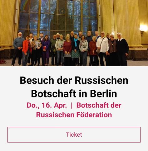 Eine Gruppe von Menschen posiert vor einem großen Buntglasfenster. Darüber liegt Text, der einen Besuch der russischen Botschaft in Berlin am 16. April ankündigt.