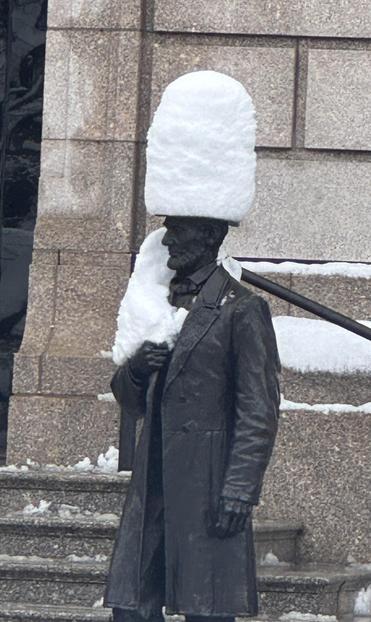 Bronze statue of Abraham Lincoln with a great cylinder of snow atop his head.