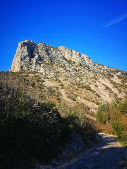 Photo en contre plongée d'une falaise/petit mont très rocailleux depuis un chemin de randonnée dans la garrigue
