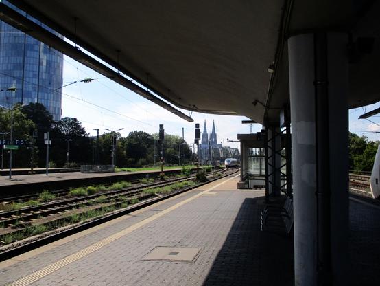 Photo prise depuis un quai de la gare de Köln-Messe-Deutz sur les voies envahies de végétation, dans le fond, on distingue le célèbre pont ferroviaire du Hohenzollern qui mène à la gare principale de Köln-Hbf et la non moins célèbre cathédrale qui est juste à côté de la gare. A gauche de la photo, une tour de verre est également visible. 

Photo taken from a platform of Köln-Messe-Deutz station on overgrown tracks, in the background we can see the famous Hohenzollern railway bridge which leads to the main station of Köln-Hbf and the no less famous cathedral which is right next to the station. To the left of the photo, a glass tower is also visible.