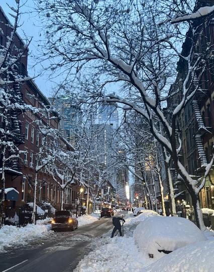 Midtown Manhattan co-ops and condos, trees covered with snow, piles of snow on parked cars. Man shoveling snow in the distance.