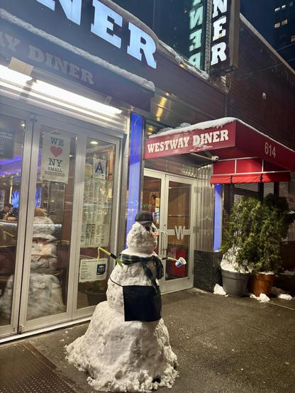 A sidewalk snowman, in front of a NYC diner.