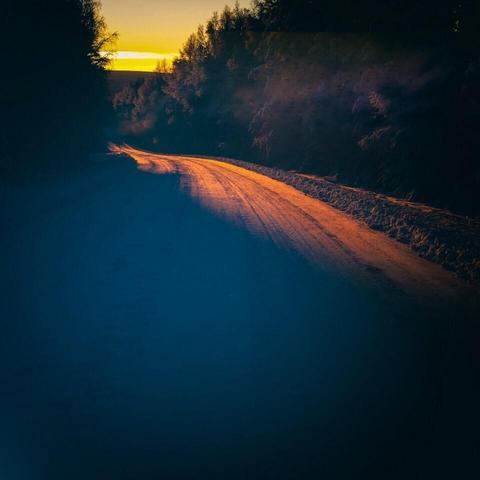 Solens strålar når över vägens krön och lyser upp den snötäckta vägen