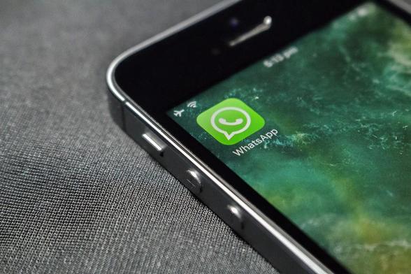 Smartphone mit grünem WhatsApp-Logo auf grauem Hintergrund, leicht schräg aufgenommen.