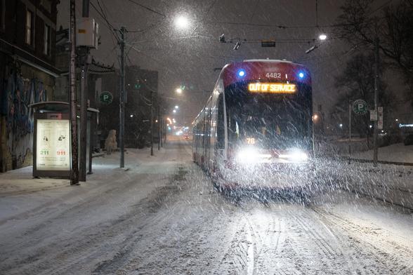 view of a 506 Carlton streetcar with out of service sign, and no traffic around at 1am.  It's snowing heavily and bright in the headlights.  Another streetcar came 7 minutes later.
