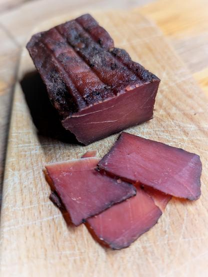 Auf einem Holzbrett liegt ein dunkelrotbrauner Block Tofu-Schinken, daneben mehrere dünn geschnittene Scheiben mit fester, fleischähnlicher Struktur. Foto: Gartenpoet, Johann Seidl