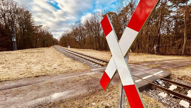 Eisenbahnschranke vor einer Bahnstrecke im ländlichen Gebiet, gelblich-braunes Feld im Vordergrund.