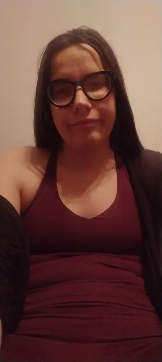 me i have long dark hair im wearing black-rimmed cateye lense glasses, a nose ring, and a purple tank top and leggings, with a black cardigan draped over her left shoulder and lower on the right arm