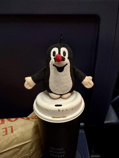 Ein kleines Plüschmaulwurf steht auf einem sehr großen Kaffeebecher. Links daneben liegt eine Tüte von Le Crobag.