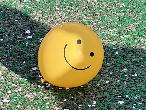 Gelber Ballon mit Smiley auf Konfetti-besprengtem Boden