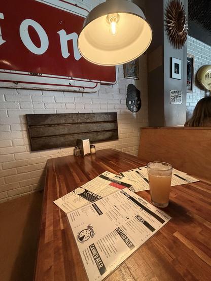 Table in a restaurant with menus a a pint of beer. Signs on the wall.