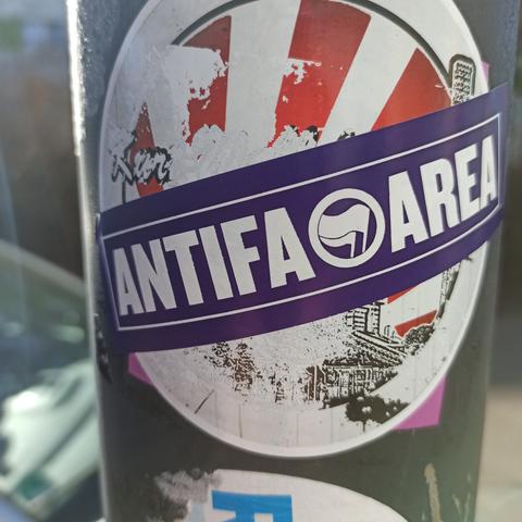 Sticker auf Laternenmast ein Antifasticker klebt über einen Sticker des Fußballklubs HFC auf dem Sticker ist zu lesen Antifa Area