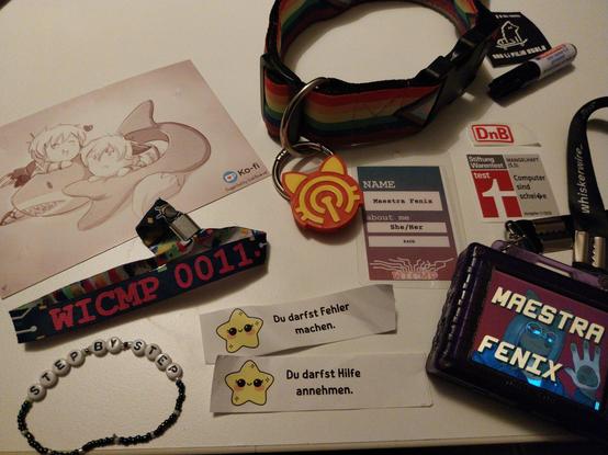 Photo "collage" of some items brought to / gotten at WICMP11

From left to right:
- Chaos Postal with art from Foxhat ( two chibi furry characters playing around a big shark plushie )
- WICMP entry wristband
- "Step by step" mental health wristband
- Rainbow pride collar ( with NFC tag chip to it, in the form of a cat, yellow and red )
- "You are allowed to do mistakes" mental health paper
- "You are allowed to accept help" mental health paper
- WICMP entry tag with my alias ( Maestra Fenix ), pronouns ( She/Her ), and Hackspace ( K4CG )
- "DnB" sticker, in the style of DB
- "Stiftung Warentest" sticker
- Color LED digibadge, showing on screen "Maestra Fenix" and a partial pic of my fursona
- "ona li lukin e mi tawa, ona li pilin utala" sticker
- Mini marker from a very dear entity to me ❤️