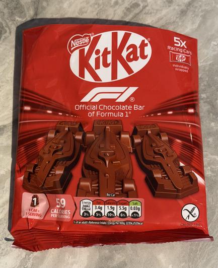 Red Nestlé KitKat multipack bag labelled “Official Chocolate Bar of Formula 1”. Front shows three chocolate bars shaped like Formula 1 cars. Text states “5x Racing Cars, individually wrapped” and “59 calories per serving”.