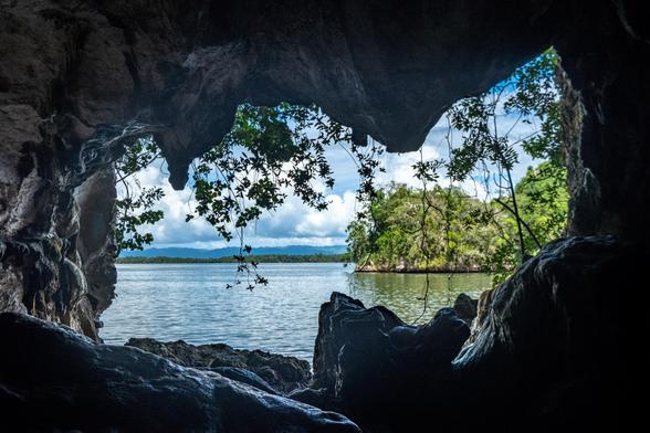 View from inside a cave looking out over a calm body of water, framed by rocky walls and lush greenery.