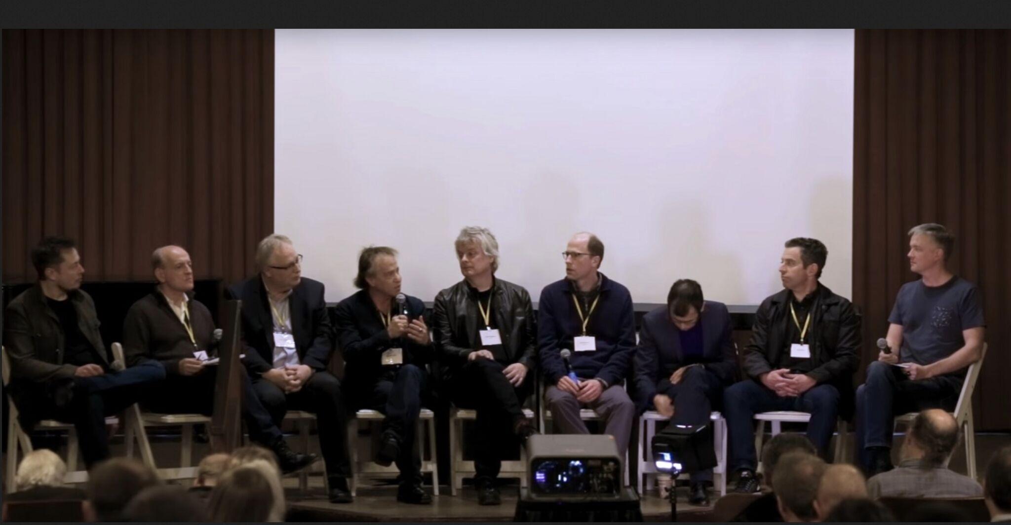 Nine, mostly white, guys on a manel on stage.