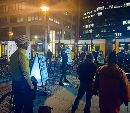 Abendliche Zwischenkundgebung bei der RespectCyclists Fahrraddemo in Berlin Mitte. Im Hintergrund ist eine Straßenbahn zu sehen, und Bürogebäude.