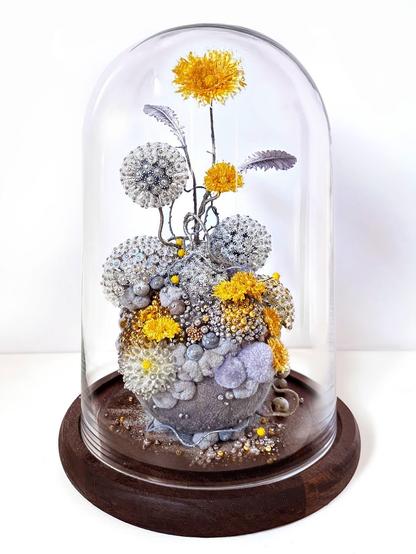 An intricate sculpture inside of a glass dome vitrine by Amy Gross of imaginative flora made from paper and beads