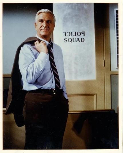 Leslie Nielsen in a promotional photo for POLICE SQUAD! Note the sign on the door.