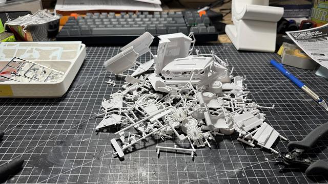 Nunu Beemax Lancia Delta S4 model kit white plastic sprues and components scattered on a cutting mat, including chassis, engine, suspension, and mechanical parts awaiting assembly