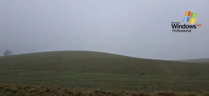 The Windows XP desktop image with logo, only that the green grass hill landscape is very foggy and desaturated.