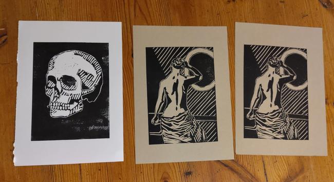 Photo of my linocut production so far. On the left a skull I made last week - black paint on white paper.
Then two prints of the woman I made this week. I had some issues centering the print on the paper. It's black paint on a beige or natural colored paper