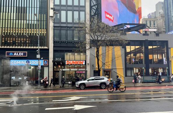 NYC 42nd St. Seen behind a bicyclist are a McDonald’s, a Dunkin’, and a space for a future Aldi’s.