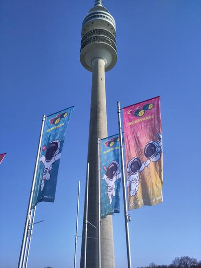 Drei große Fahnen der Messe ggbavaria vor dem Olympiaturm vor strahlend blauem Himmel.