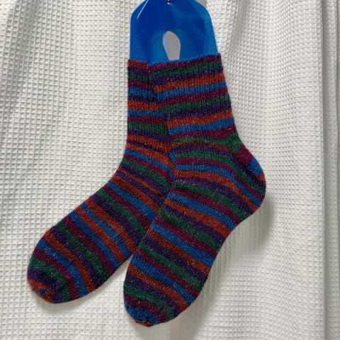 A pair of sparkly jewel toned striped socks. Hand knit and suspended on a set of blue sock blockers.