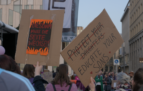 Demoschilder: "Die Scham muss die Seite wechseln" und
(durchgestrichen) "Protect your Daughters", darunter, nicht durchgestrichen "Educate your Sons"