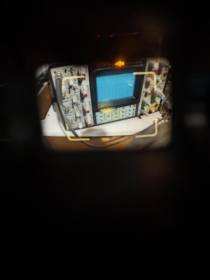 Photo prise à travers le viseur, on voit un oscilloscope et surtout le cadre lumineux correspondant à ce que vois l'objectif et une petite flèche jaune au dessus