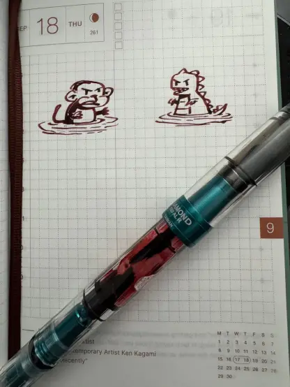 A sketch of a cartoon Kong and cartoon Zilla facing each other with menacing looks wading through a river or other body of water. Fountain pen almost out of ink sits atop the paper.