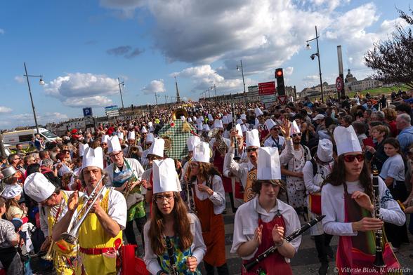 Une foule compacte dĂ©file Ă hauteur de la place de la RĂ©sistance et sâĂ©tend jusquâĂ lâarriĂšre-plan, avec une fanfare portant des chapeaux de cheffes au premier plan.