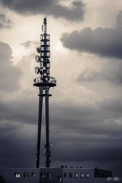 Ein Funkmast mit Parabolantennen auf einem Flachdachgebäude vor dramatisch bewölktem Himmel