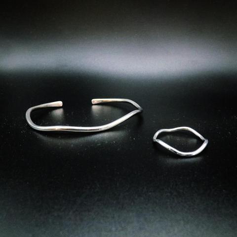 a wavy silver cuff bracelet and a similar ring on black background
