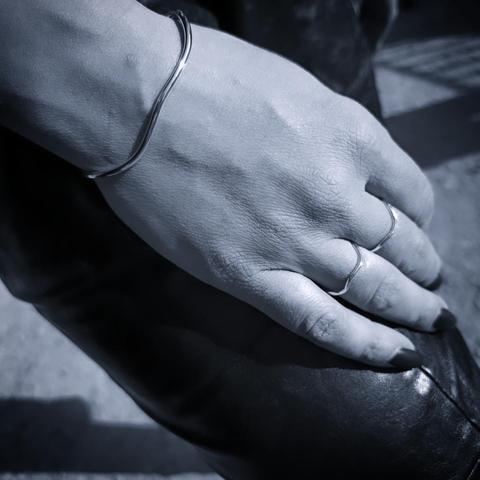 a wavy silver cuff bracelet and two similar rings worn on a woman's hand